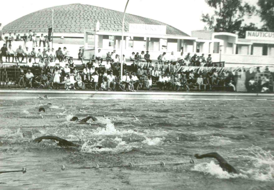 Foto antiga em preto e branco de prova de natação com arquibancada cheia