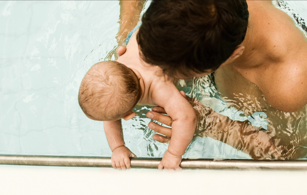 Pai segurando um bebê junto à borda da piscina aquecida